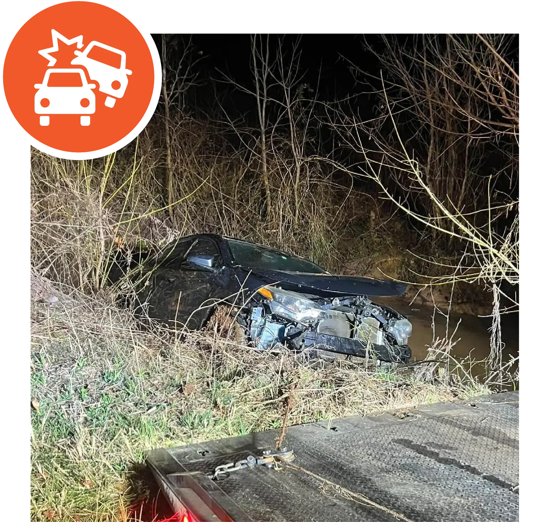 Totaled blue SUV crashed into river bank. Tow truck platform in front of it, ready to pull it out.