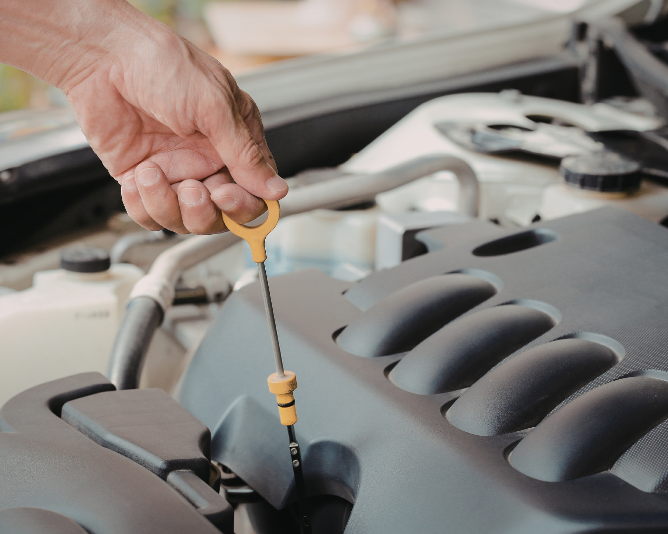 Person pulling a car’s oil dipstick to check engine oil level under an open hood.