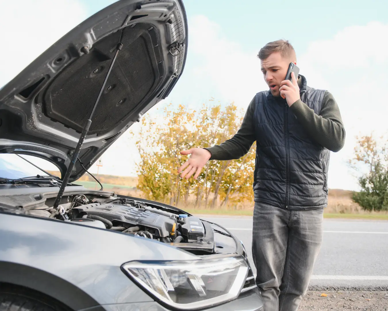Man on the phone standing beside his broken down car.