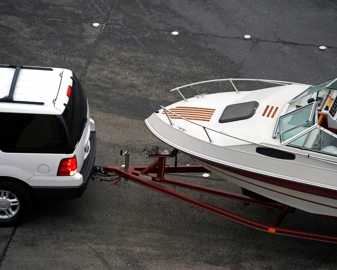 White SUV towing a boat on a trailer along a roadway, illustrating safe boat transportation and towing before a potential roadside breakdown.
