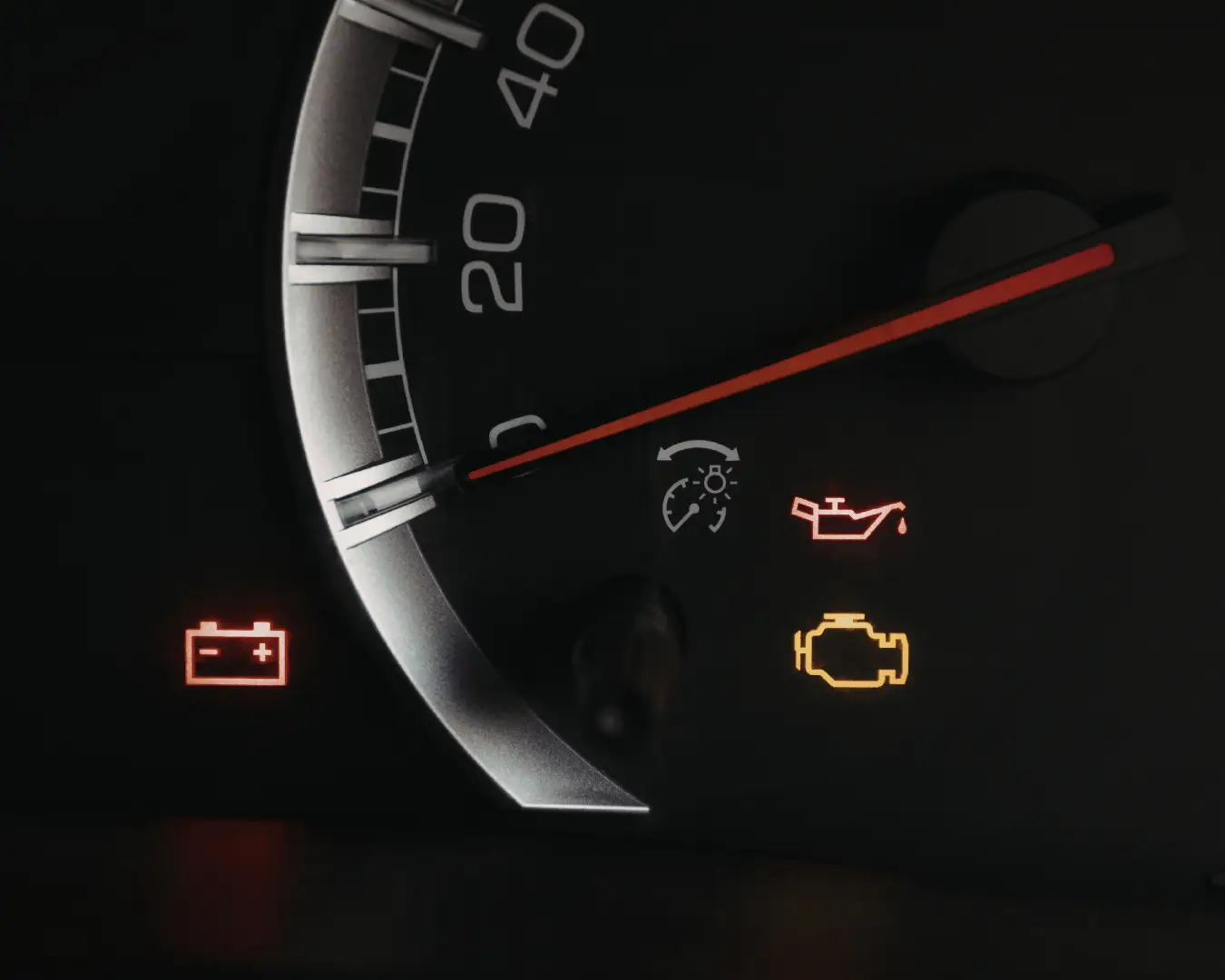 Close-up of a vehicle dashboard display showing illuminated warning icons, including a battery symbol, oil pressure can, and check engine light, next to a speedometer needle.